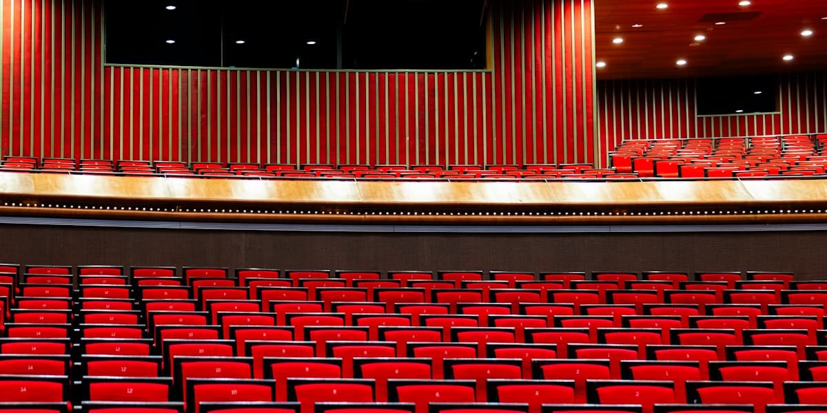 An empty auditorium of red seats facing a dark, bare stage