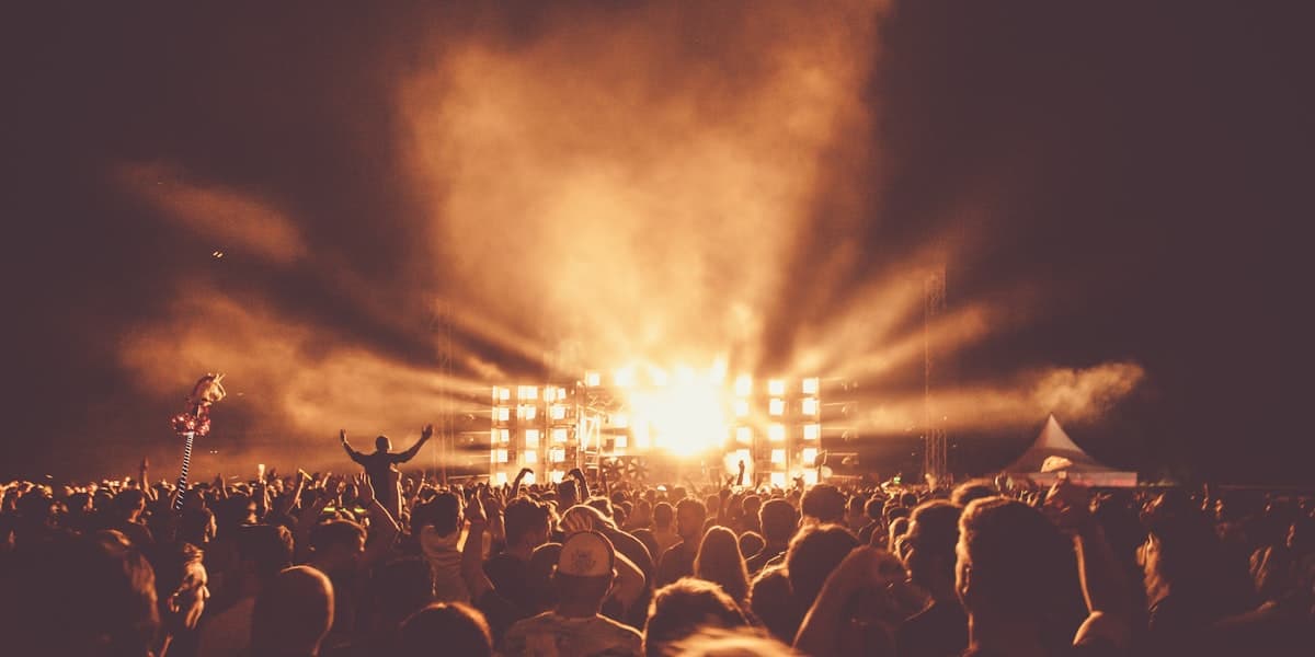 A dense festival crowd bathed in magenta stage light and smoke