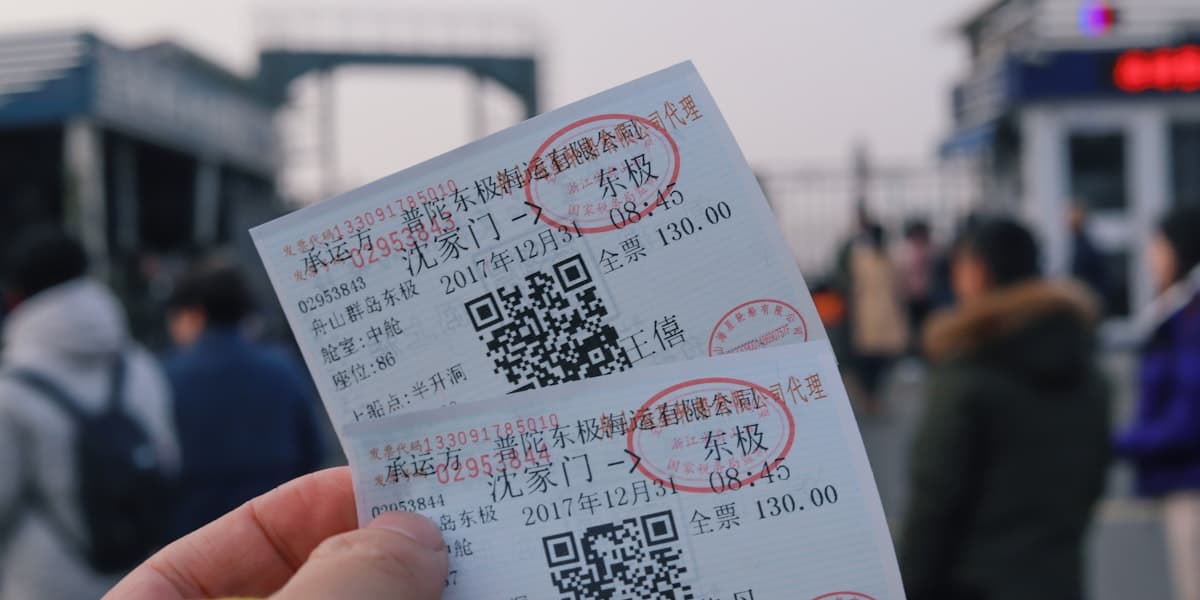 A person's hand holding two white admission tickets against a grey background