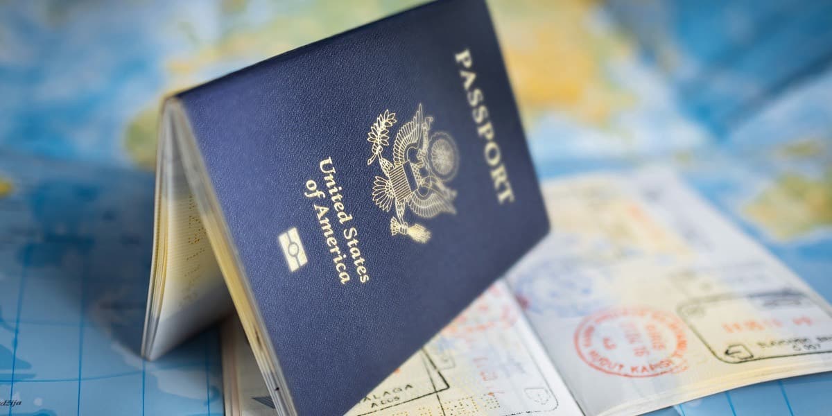 A United States passport standing open on a world map, entry visa stamps visible on the pages beside it