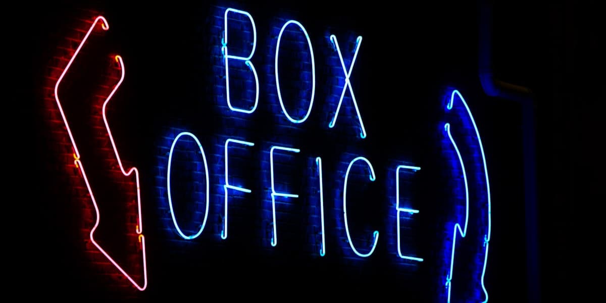 A neon Box Office sign glowing in red and blue against a dark brick wall