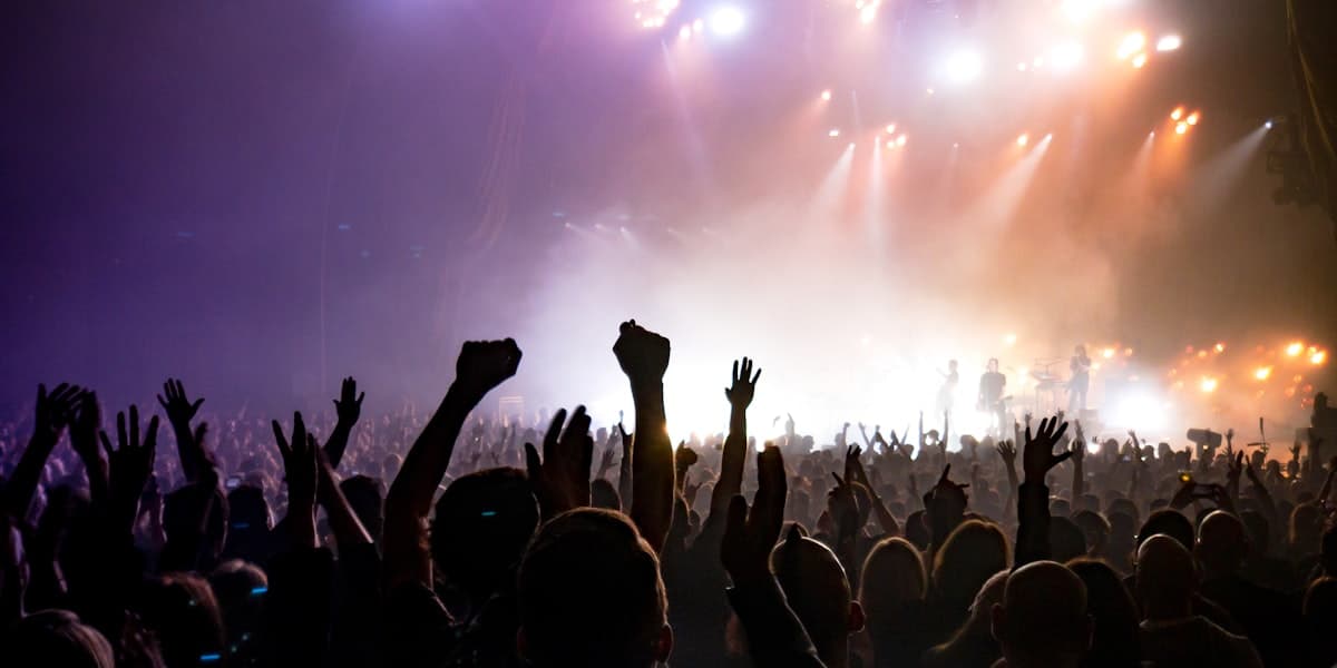 Concert crowd facing a brightly lit stage under purple and blue lights
