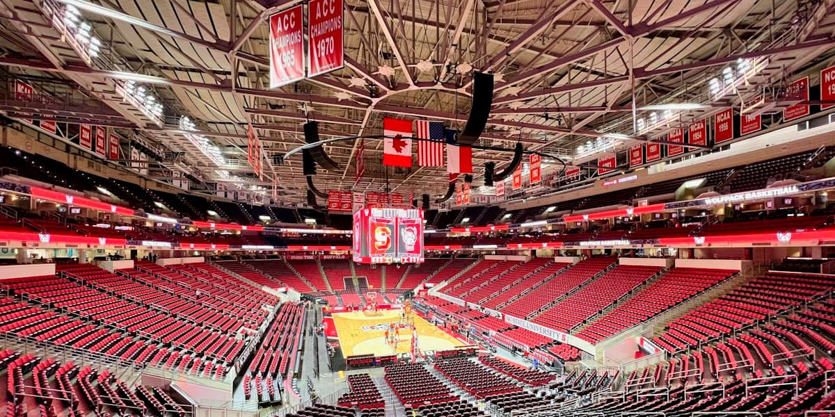 Rows of empty red seats rising on all sides of an arena bowl around a basketball court set on the floor, with championship banners hanging from the rafters