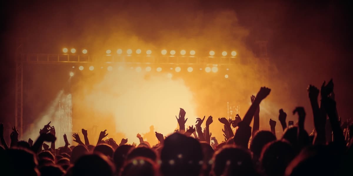 A concert crowd with raised hands silhouetted against warm amber stage lights
