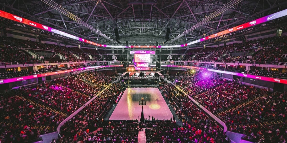 A packed indoor arena seen from the upper deck, stage lit at center