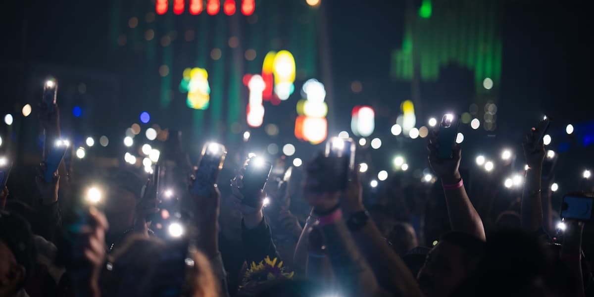 A concert crowd holding up glowing phones in the dark