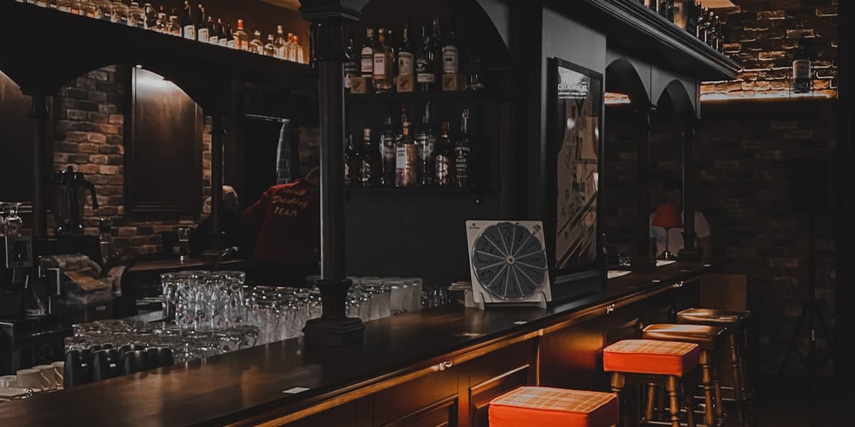 A dimly lit venue bar with stools and backlit shelves of bottles